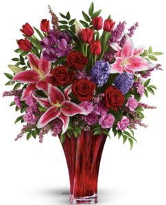 magnificent bouquet of roses, lilies, alstroemeria and more, artfully arranged in an elegant red blown-glass vase.