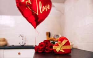 Close-up photo of a bouquet of red roses, a big balloon and a red heart-shaped box with a golden ribbon