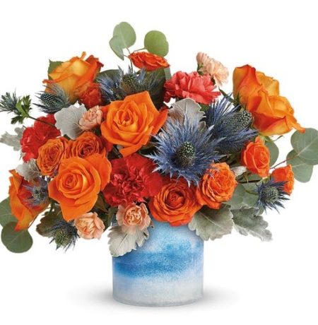 Tres chic! This high-fashion mix of bold orange roses and eye-catching blue eryngium, arranged in a frosted art glass vase, is a stand-out gift for any occasion! This chic arrangement features orange spray roses, dark orange carnations, peach miniature carnations, blue eryngium, seeded eucalyptus, and dusty miller. Delivered in a Blue Skies Color Frost Art Glass cylinder.