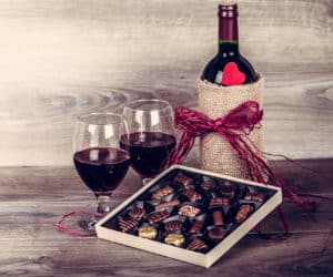 Bottle of wine, assorted box of chocolate, and two red wine glasses